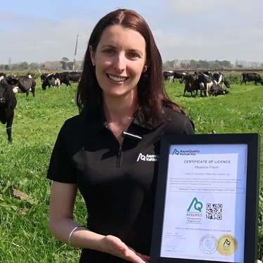 AQ employee holding an AQ certificate in a farm paddock with cows and grass